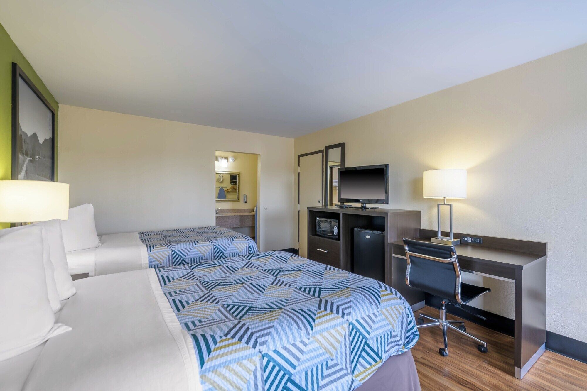 A hotel room with two beds, a desk, a television, and a desk lamp.