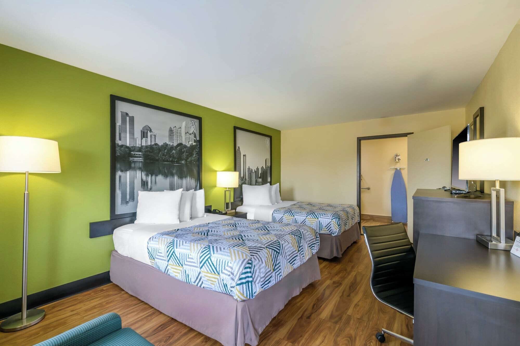 Habitación de hotel con dos camas, un escritorio y una silla. Hay dos lámparas y un cuadro en la pared.