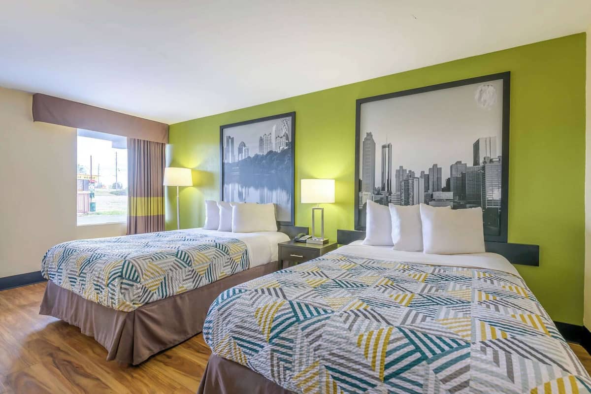 A hotel room with two beds, green walls, cityscape artwork, and a window with curtains.