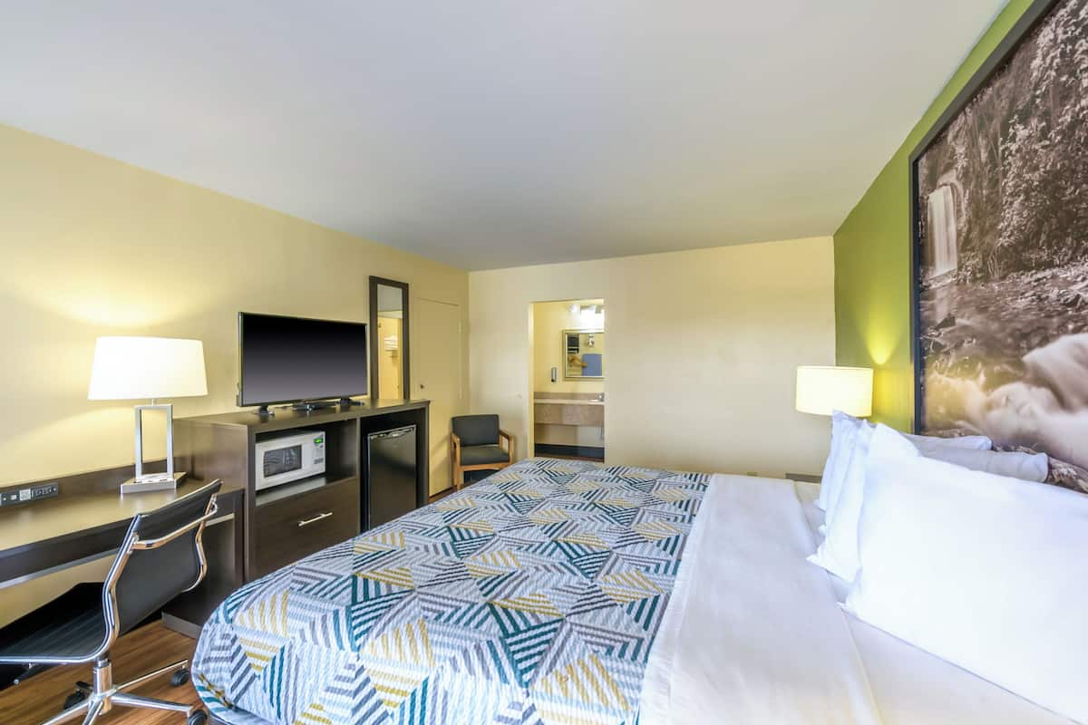 A hotel room with a bed, desk, chair, TV, and a painting on the wall.