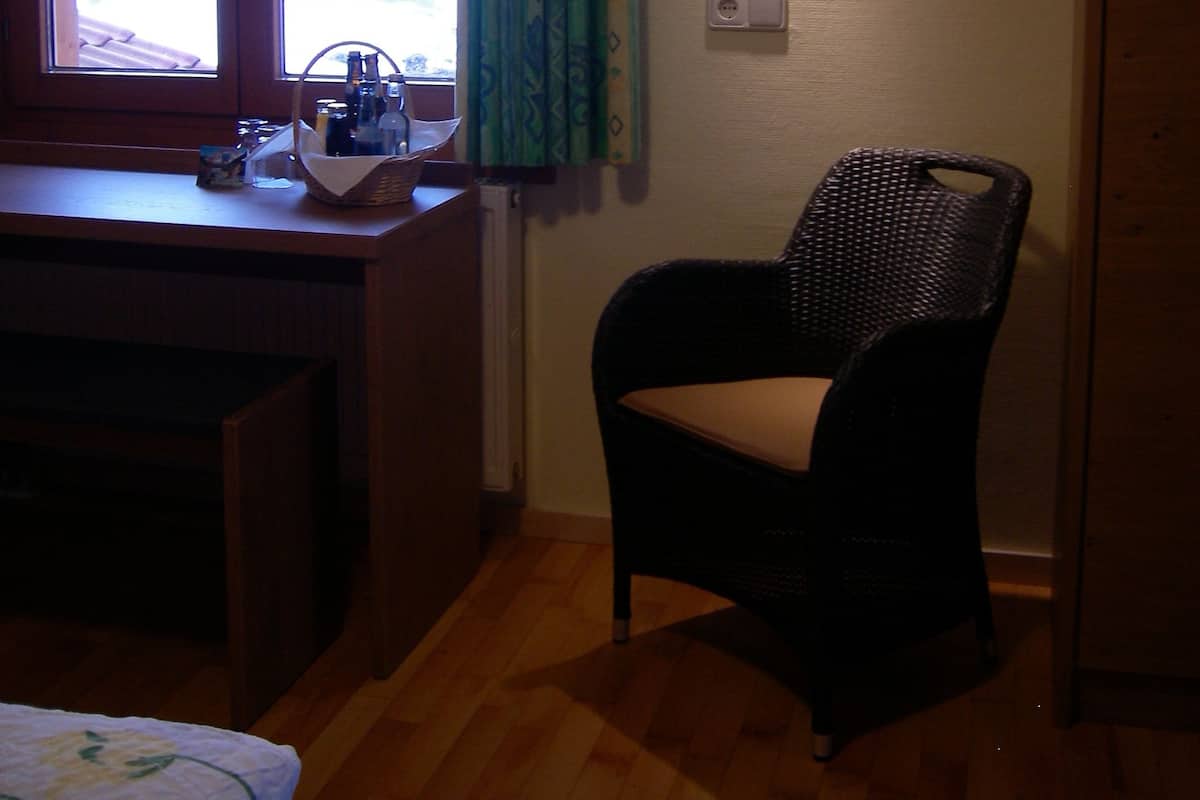 A room with a wooden desk, a wicker chair, a window with a curtain, and a wall-mounted light fixture.