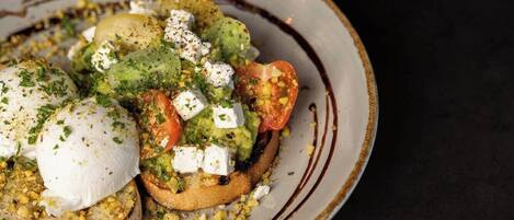 Une assiette de bruschettas garnies de guacamole, de tomates et de fromage, accompagnée d’une tasse de café.
