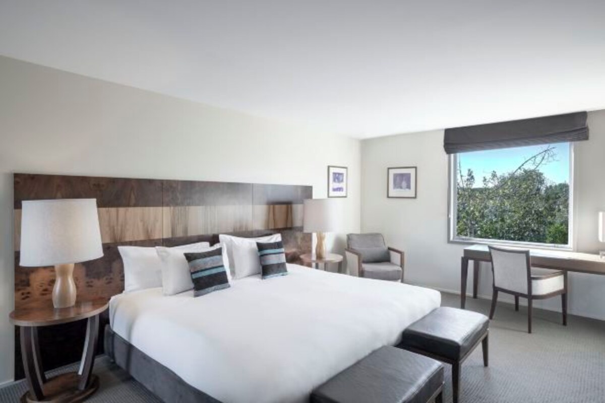 A hotel room with a large bed, a desk, two chairs, a window with a view, and a headboard.