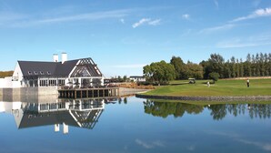 A lakeside building with a dock, a golf course, and a reflection in the water.
