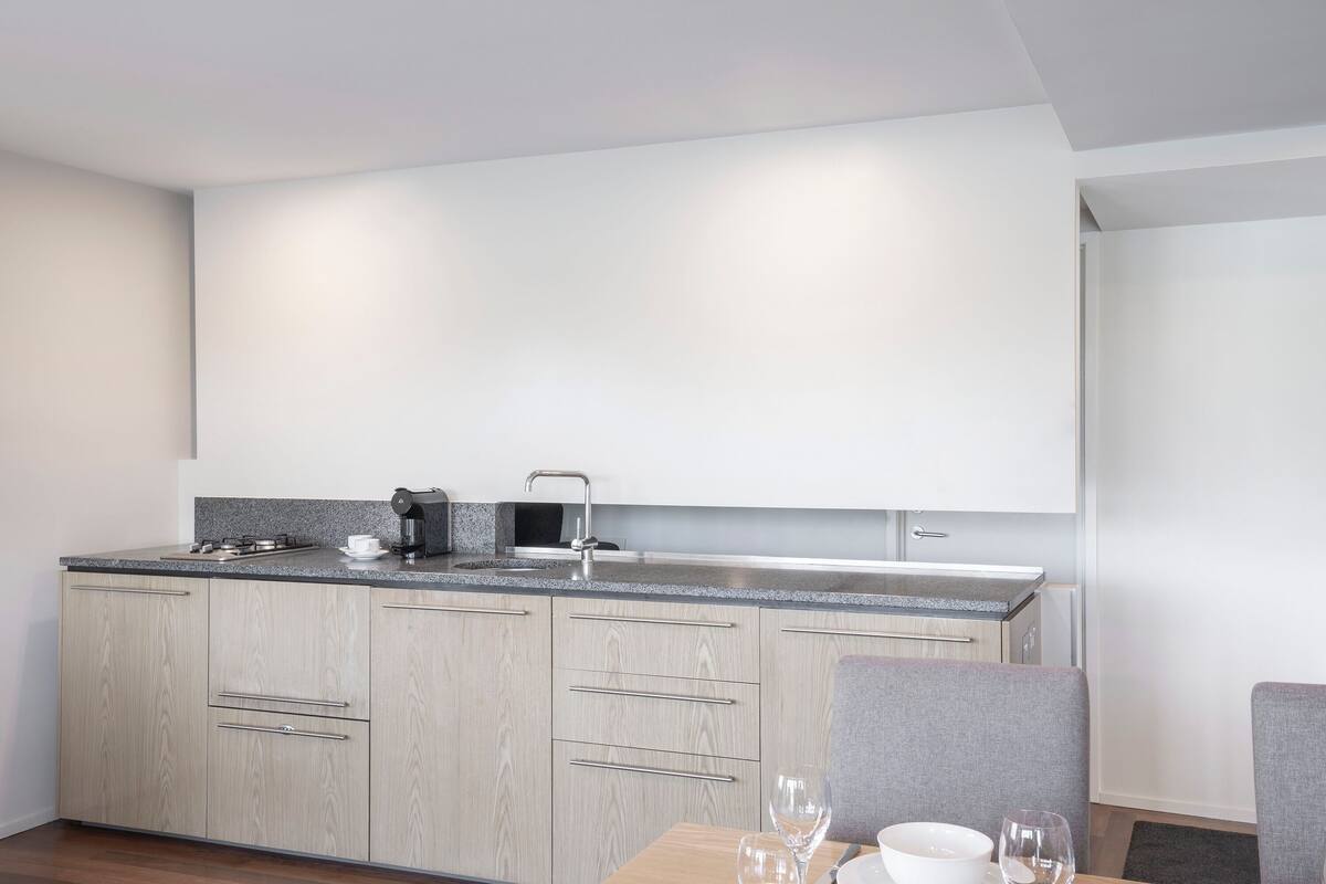 A modern kitchen with light wood cabinets, a granite countertop, and a built-in sink.