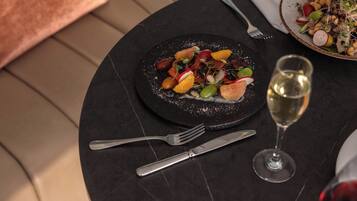 Une table de salle à manger ronde, avec une assiette noire contenant de la nourriture, un verre à vin et des couverts.