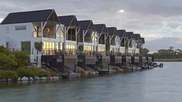 A row of white buildings with dark roofs, connected by wooden walkways over water.