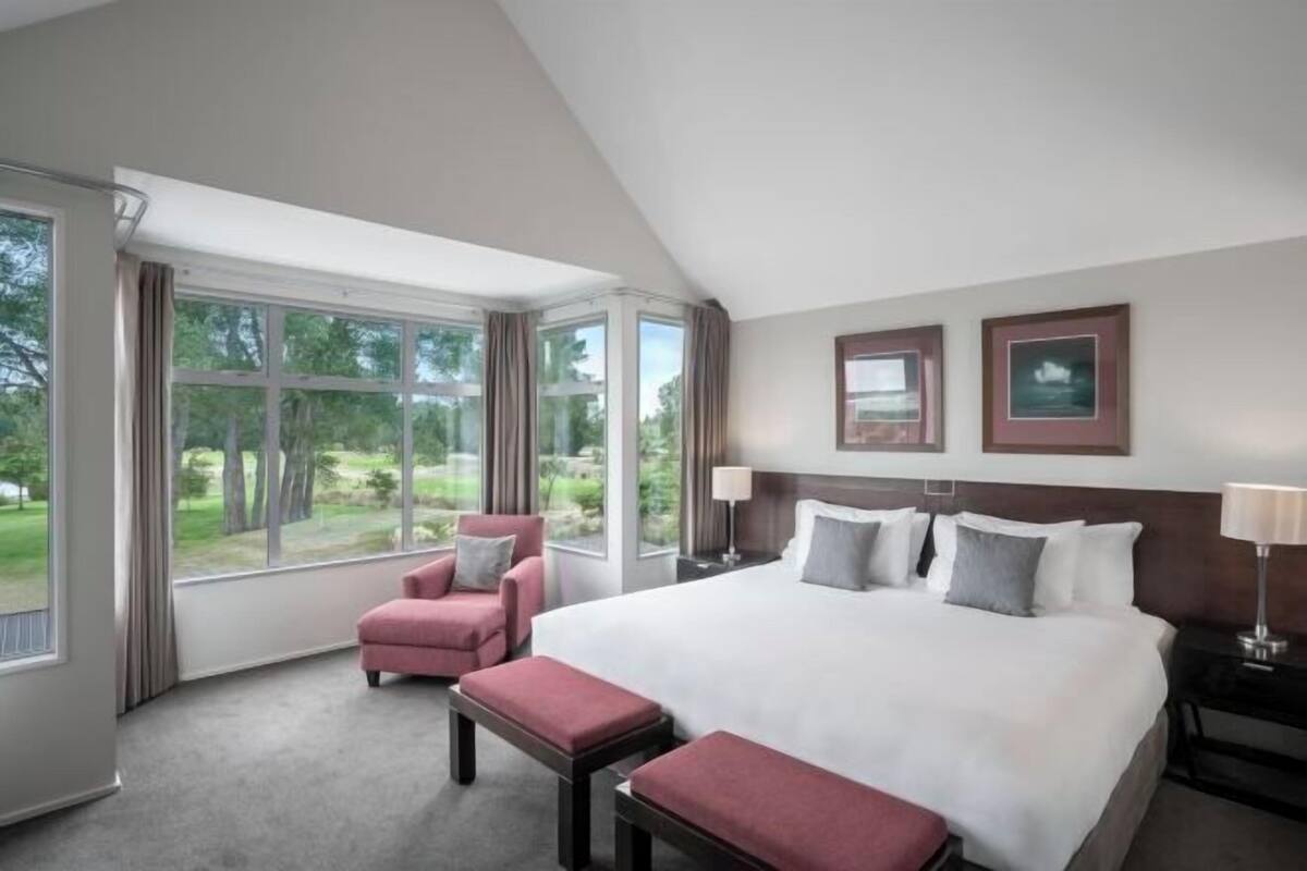 A hotel room with a large bed, a chair, a bench, and a view of the outdoors.