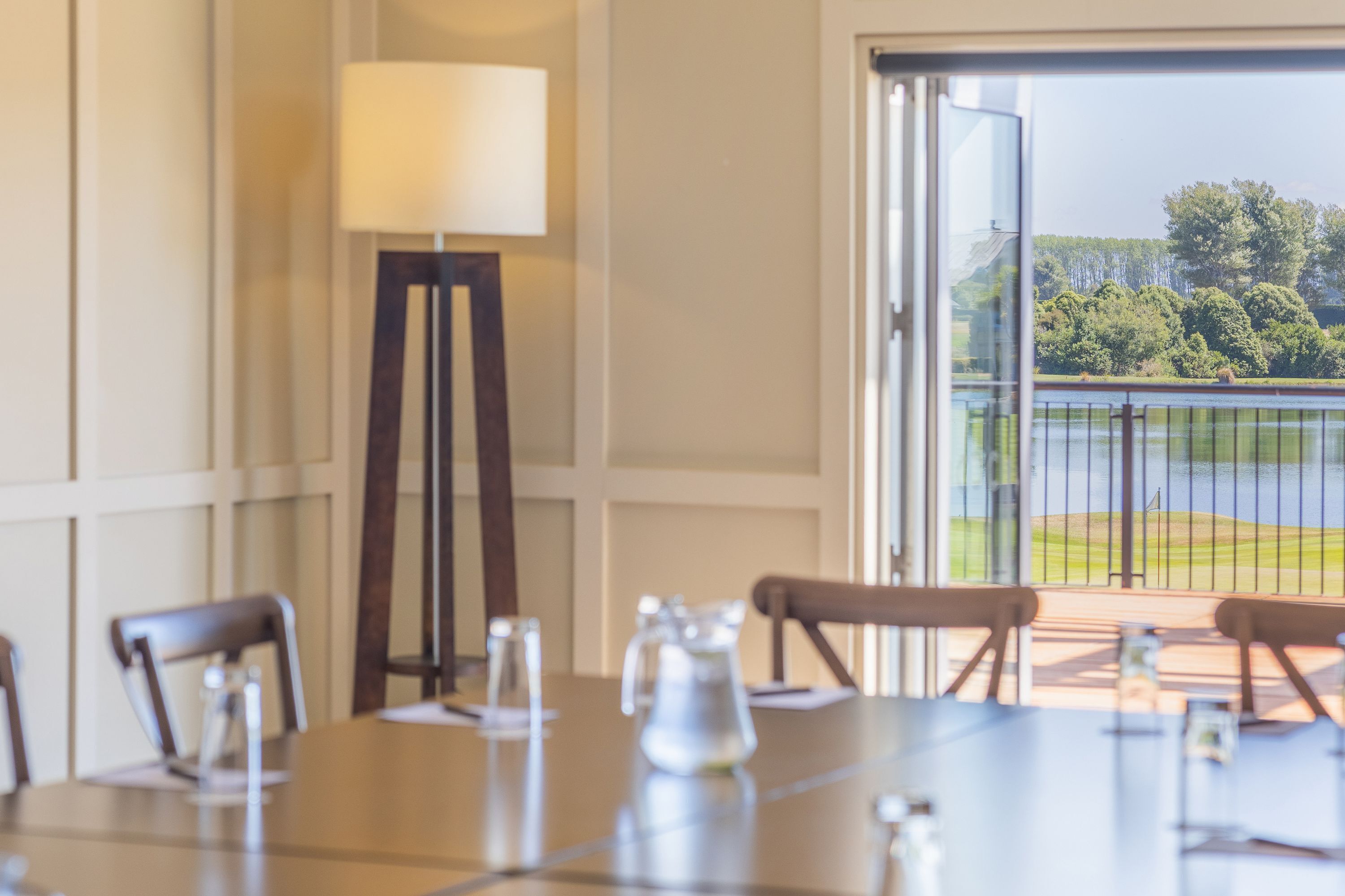 A dining area with a table set for four, a floor lamp, and a view of a golf course through a glass door.