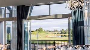 Un comedor con mesas dispuestas para una comida, amplias ventanas que ofrecen vistas a un campo de golf y un techo decorativo con estructuras similares a hojas.