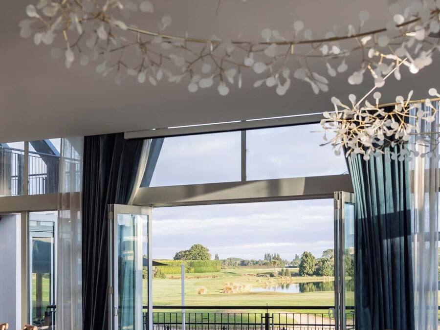 A dining area with tables set for a meal, large windows offering a view of a golf course, and a decorative ceiling with leaf-like structures.