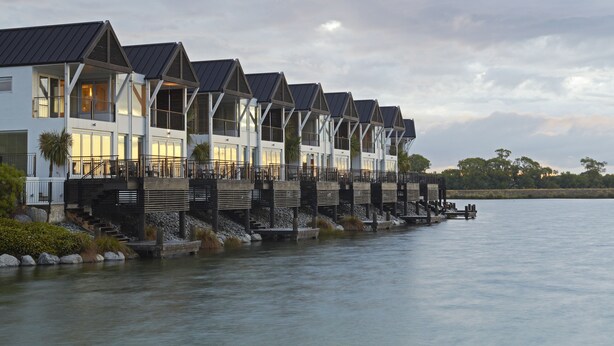 A row of modern waterfront homes with balconies, connected by a dock.
