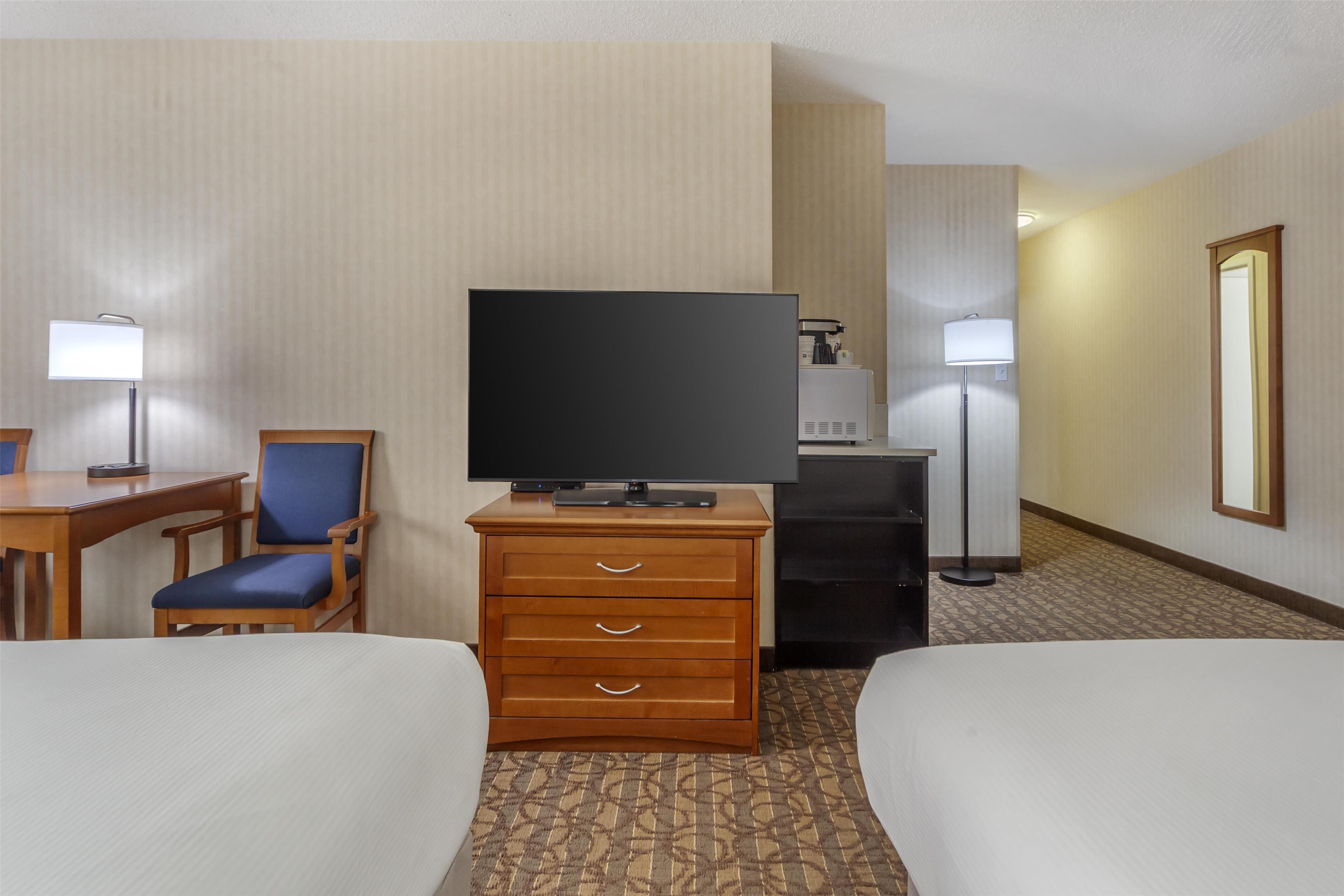 A hotel room with two beds, a desk with a chair, a television, a dresser, and a lamp.