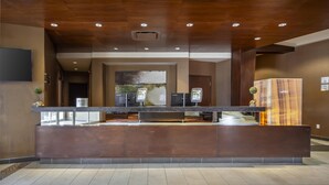 A reception area with a wooden reception desk, a large painting on the wall, and a television mounted on the wall. - Best Western Cold Lake Inn (Cold Lake)