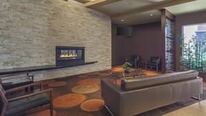 A modern lobby with a stone wall, a fireplace, leather seating, and a large window. - Best Western Cold Lake Inn (Cold Lake)
