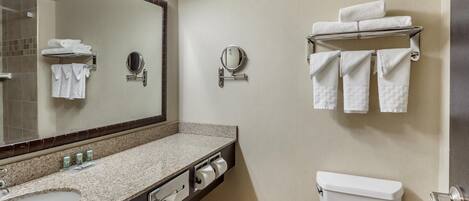A modern bathroom with a granite countertop, a sink, a mirror, a toilet, and towel racks.