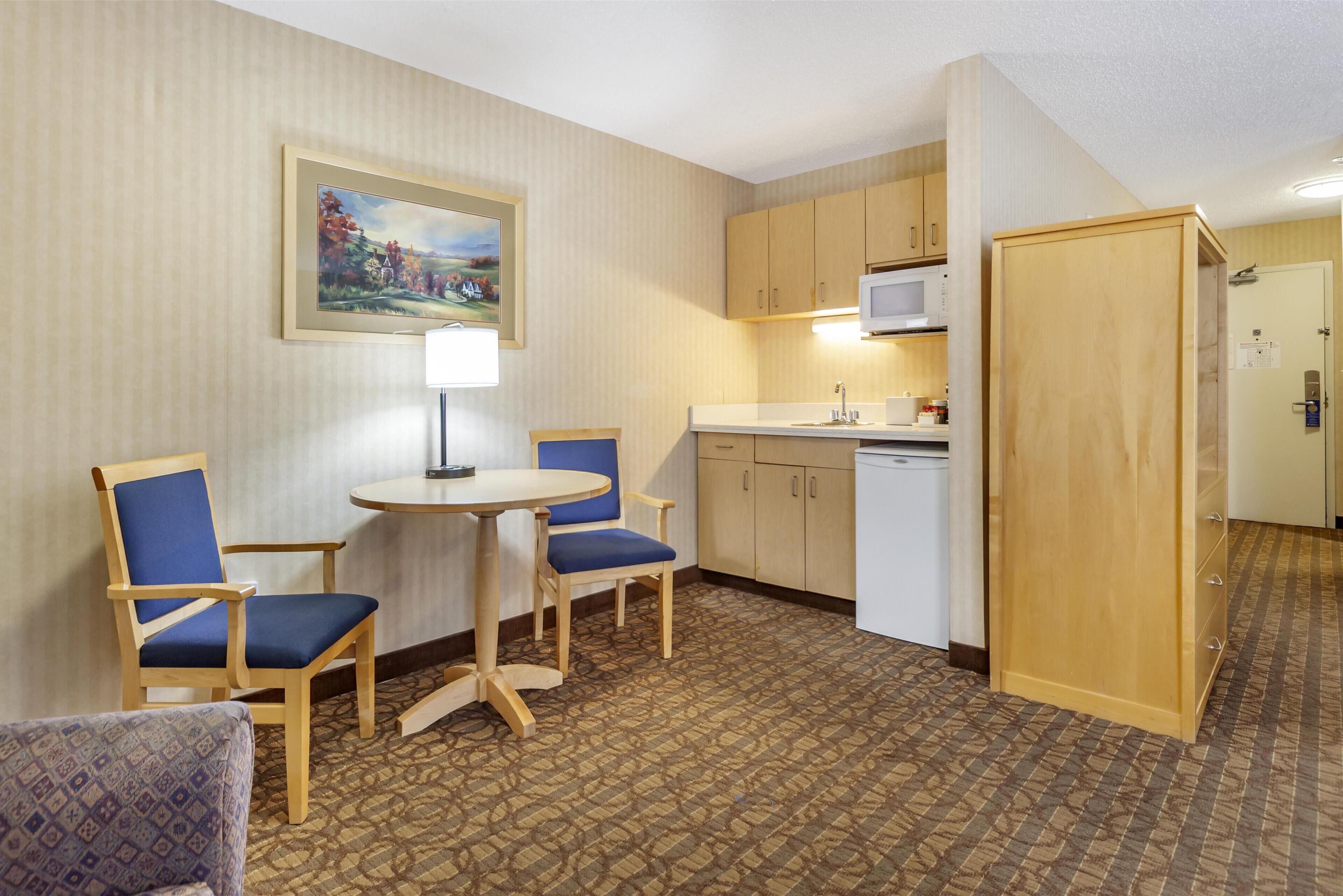 A compact hotel room with a dining table, two chairs, a microwave, a sink, and a cabinet.