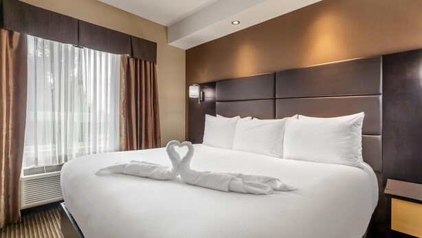 A hotel room with a large bed, a headboard with built-in lighting, and a window with curtains. - Best Western Cold Lake Inn (Cold Lake)