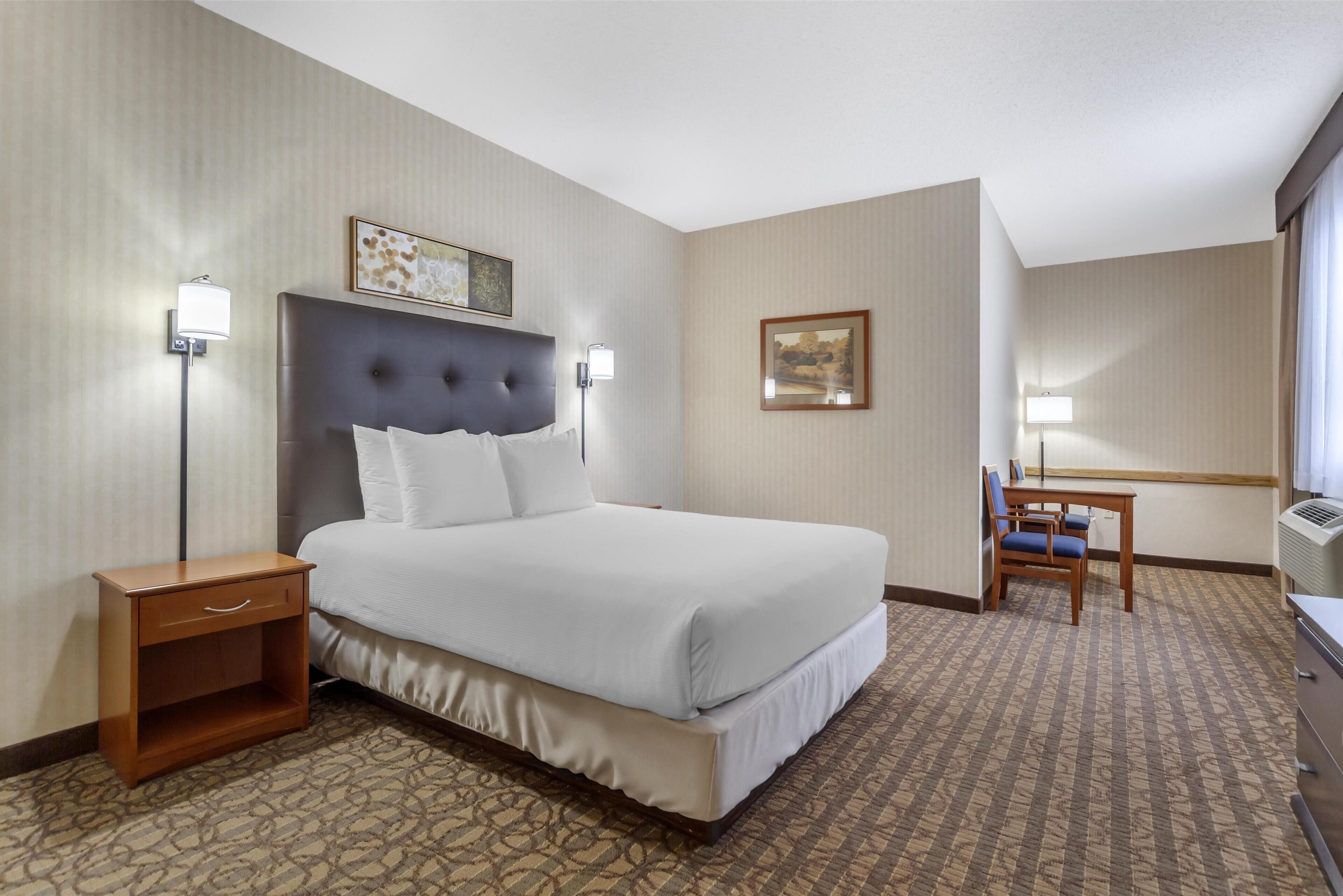 A hotel room with a large bed, bedside tables, a desk with chairs, and a patterned carpet.