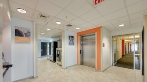 A clean, modern hallway with a tiled floor, an elevator, and a sign indicating an exit. - Motel 6 Brampton, ON - Toronto (Brampton)