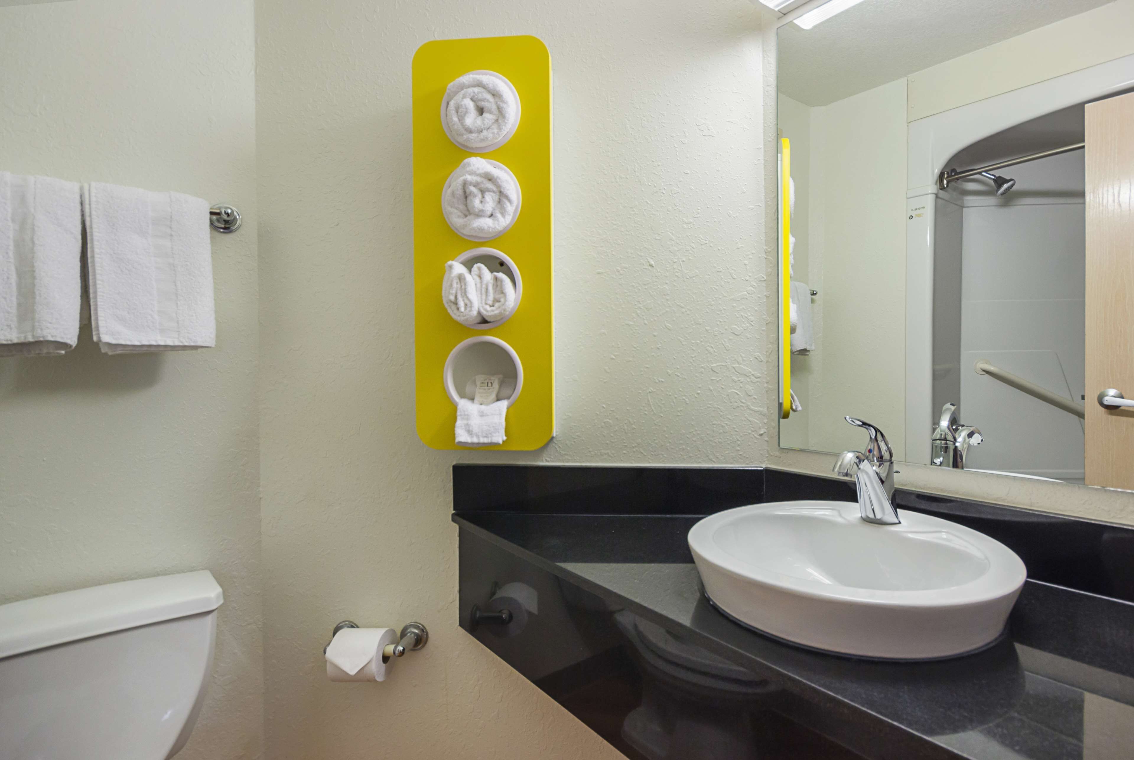 A bathroom with a white sink, a mirror, and a yellow towel rack with four towels.