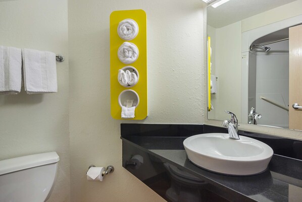 Un baño con un lavamanos blanco, un espejo y un toallero amarillo con cuatro toallas.