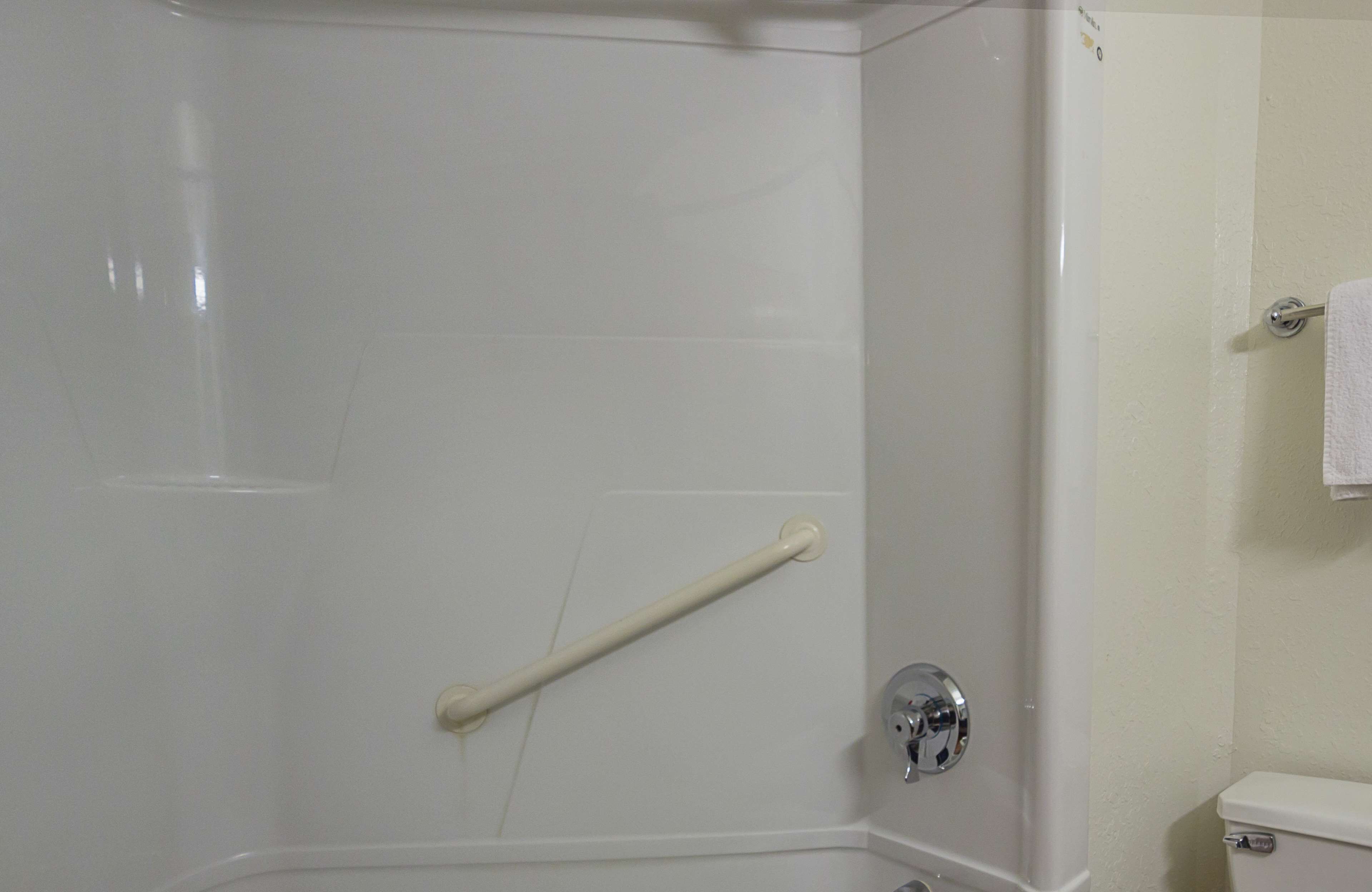 Une salle de bain avec une cabine de douche blanche, une barre d’appui, des toilettes et une serviette suspendue à un porte-serviettes.