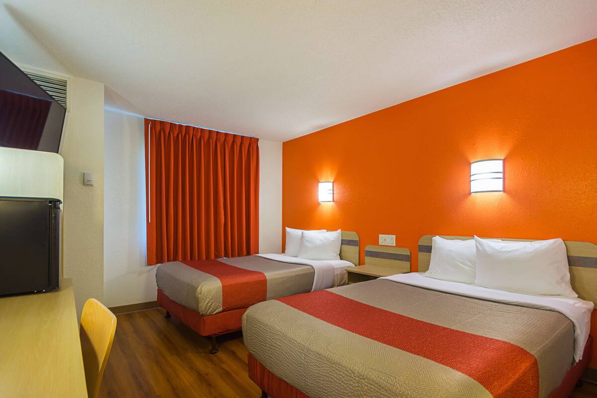 A hotel room with two beds, a desk, and a refrigerator.