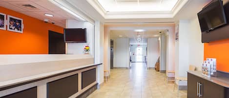 Un área de recepción con mostrador, televisor montado en la pared y un pasillo que conduce a otras habitaciones.
