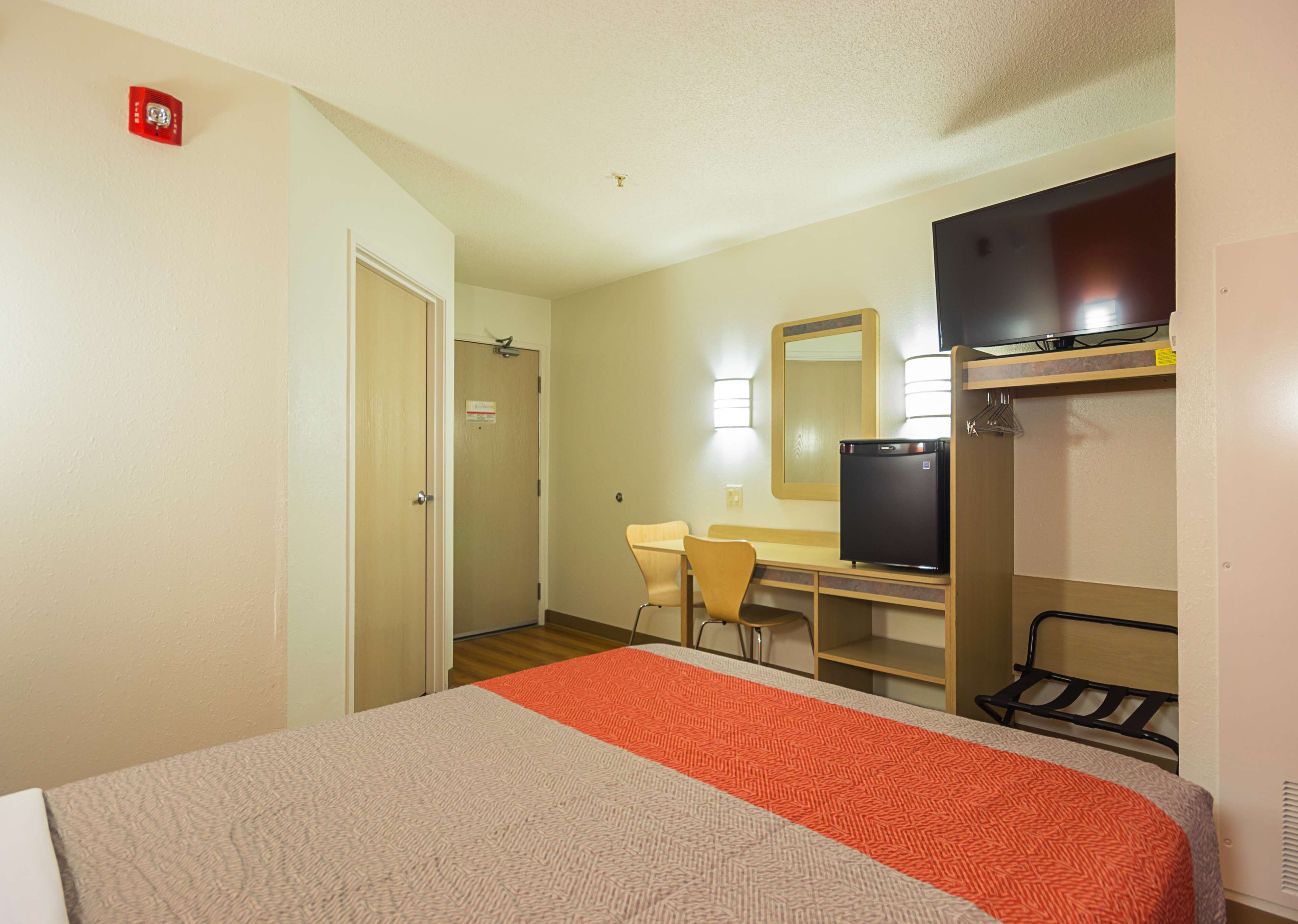 A hotel room with a bed, a desk, a chair, a television, and a small refrigerator.