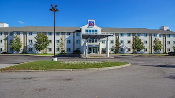 Un hotel de varios pisos con un llamativo logotipo con el número '6' en el edificio, una entrada cubierta y un estacionamiento al frente.