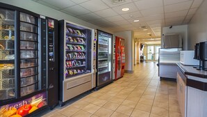 A clean, well-lit corridor with vending machines offering snacks and beverages, a microwave, and a refrigerator. - Motel 6 Whitby, ON - Toronto East (Whitby)