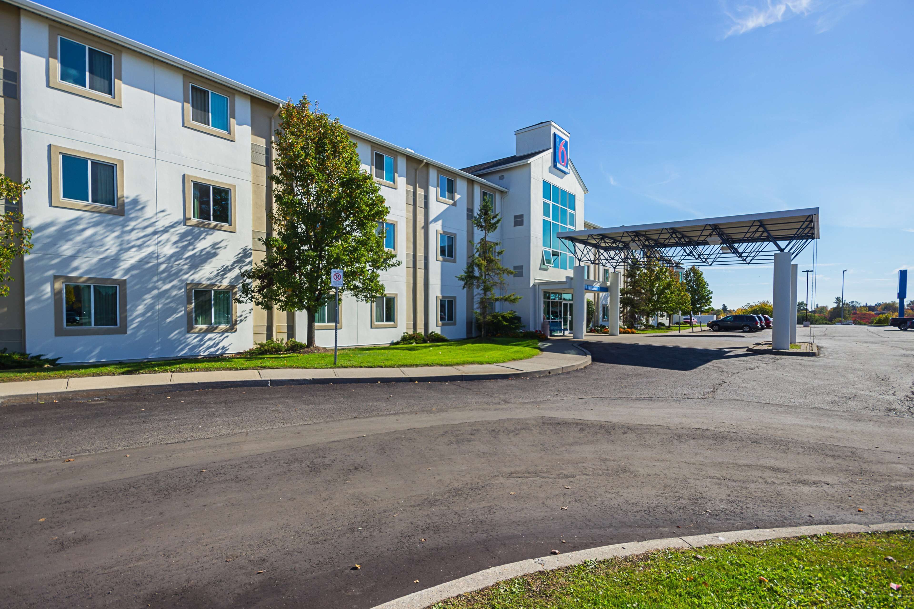 A modern hotel with a covered parking area, a well-maintained lawn, and a clear blue sky.