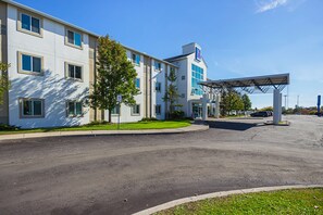 A modern hotel with a covered parking area, a well-maintained lawn, and a clear blue sky.