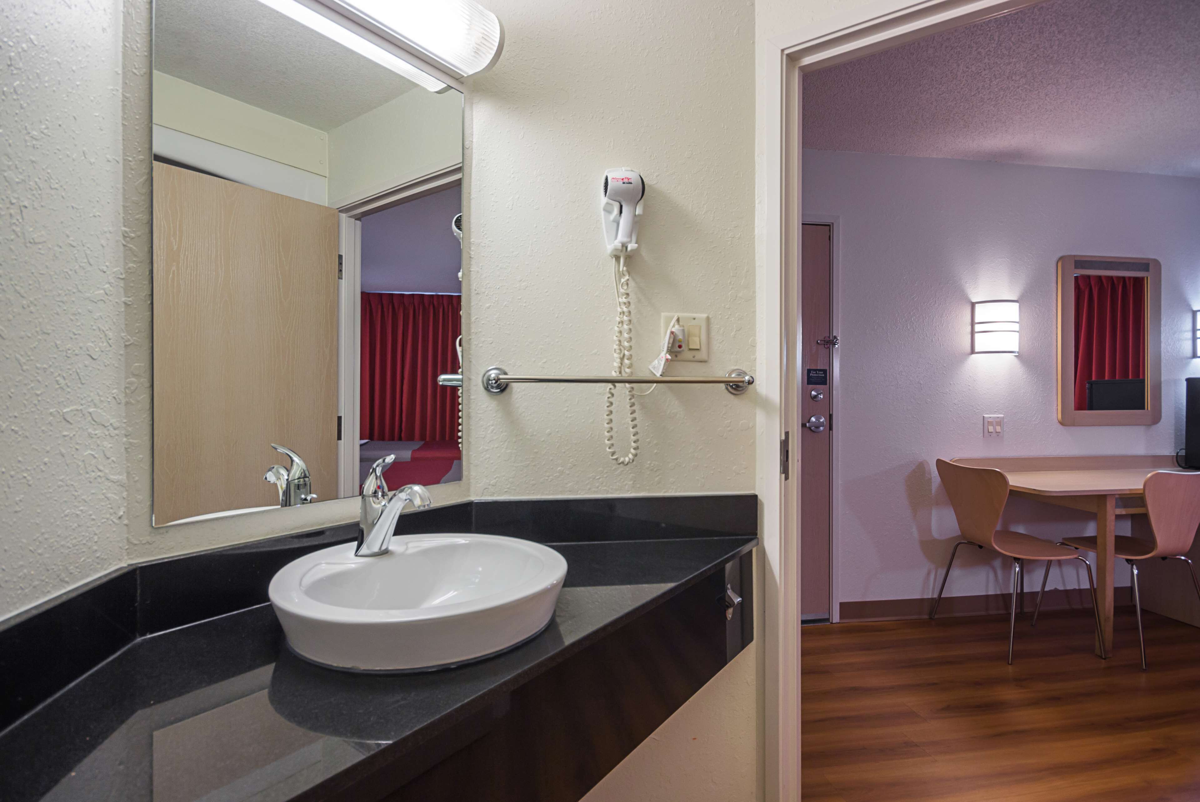 A hotel bathroom with a sink, mirror, hairdryer, and a telephone.