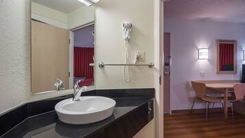 A hotel bathroom with a sink, mirror, hairdryer, and a telephone.