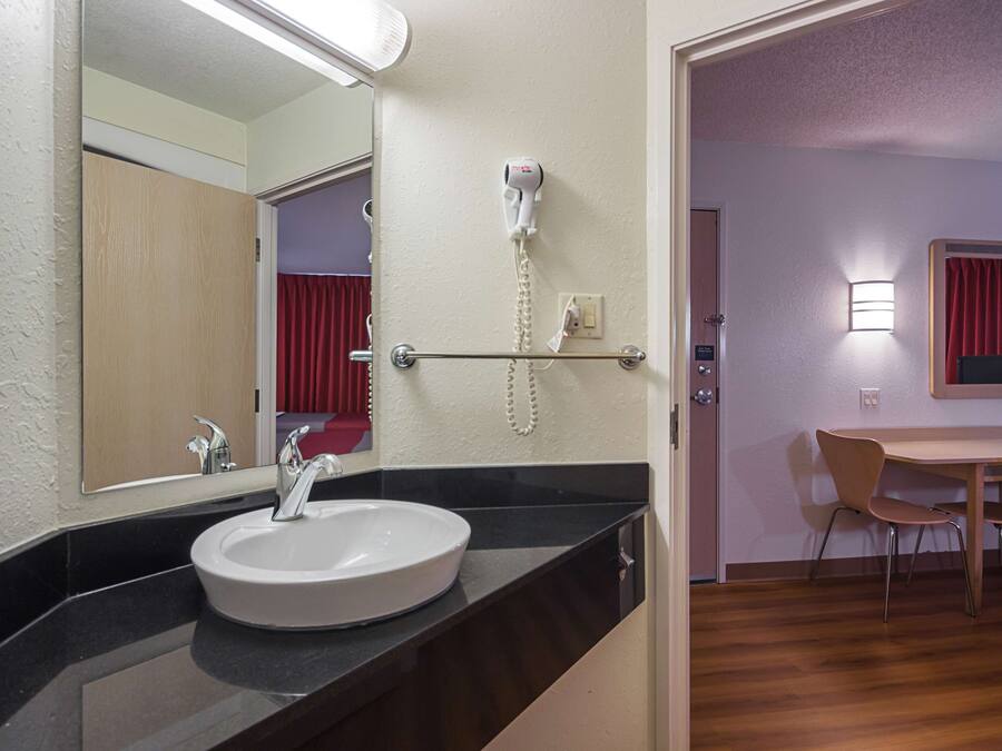 A hotel bathroom with a sink, mirror, hairdryer, and a telephone.