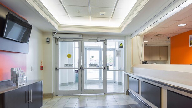 A modern interior with a reception area, a glass door entrance, and a counter. - Motel 6 Whitby, ON - Toronto East (Whitby)