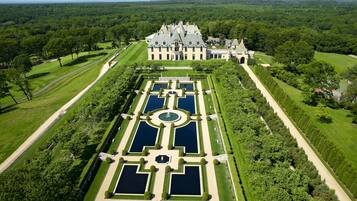 Vista aérea de uma grande e histórica propriedade com um jardim formal, incluindo um elemento aquático simétrico e gramados bem cuidados.