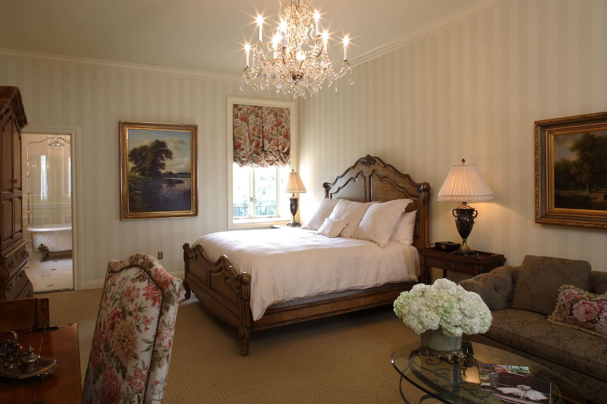 Une chambre à coucher avec un grand lit, un lustre, un canapé et une table basse sur laquelle est posé un vase de fleurs.