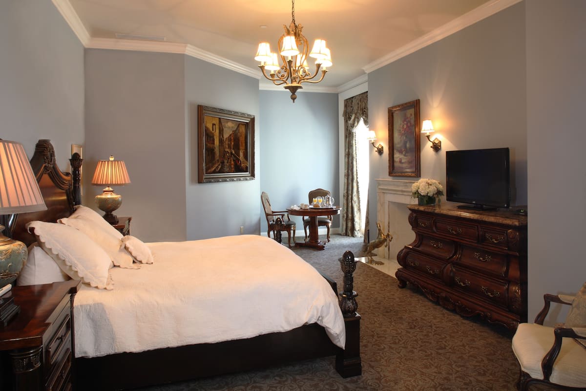 Une chambre d’hôtel avec un grand lit, une commode, une télévision et un lustre.