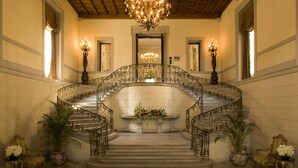 A grand staircase with ornate metal railings, a chandelier, and potted plants. - Oheka Castle Hotel & Estate (Huntington)