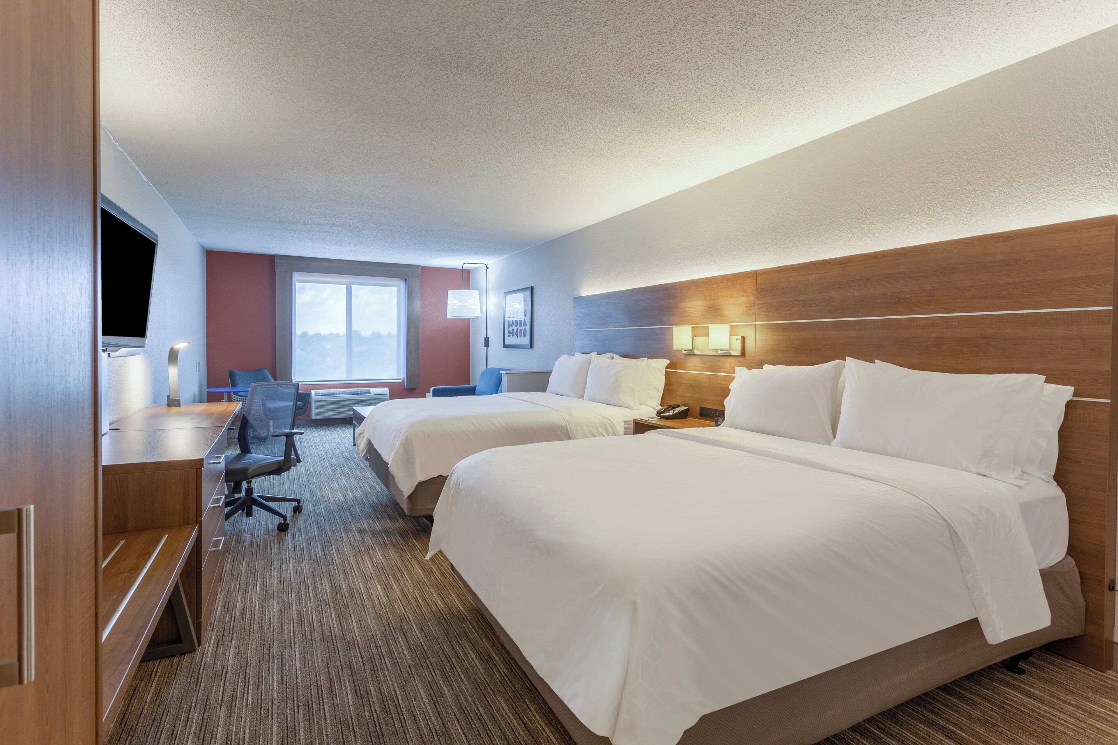 A hotel room with two beds, a desk, a chair, a TV, and a window.