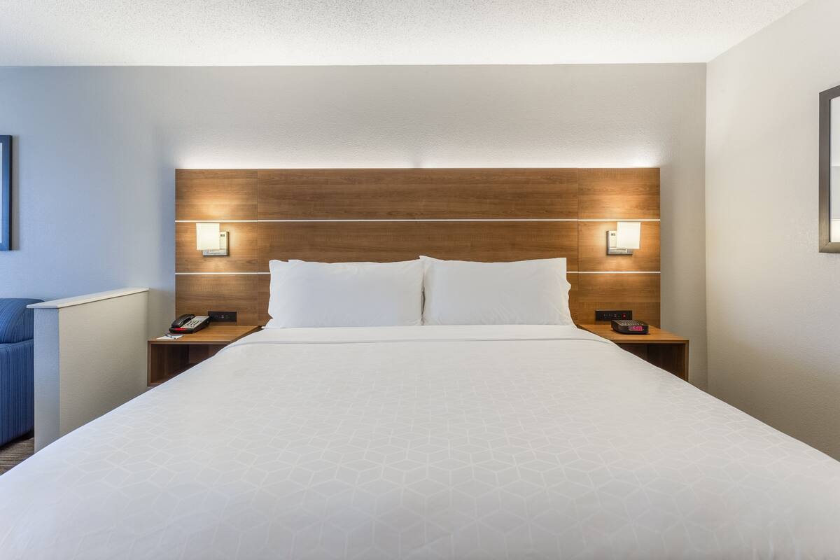 A hotel room with a large bed, wooden headboard, bedside lamps, and a telephone on the nightstand.