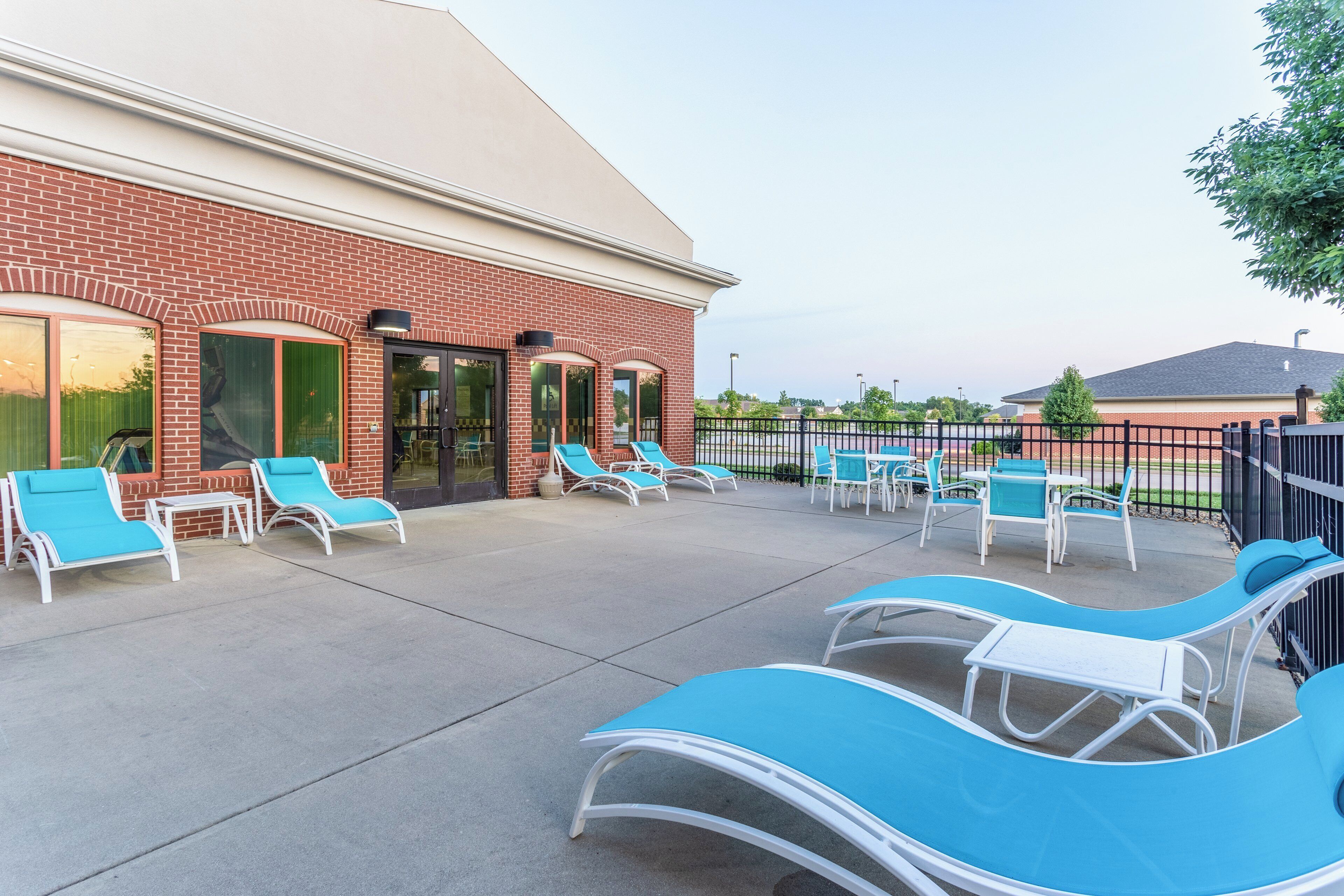 An outdoor seating area with lounge chairs and tables, a brick building with large windows, and a clear sky.