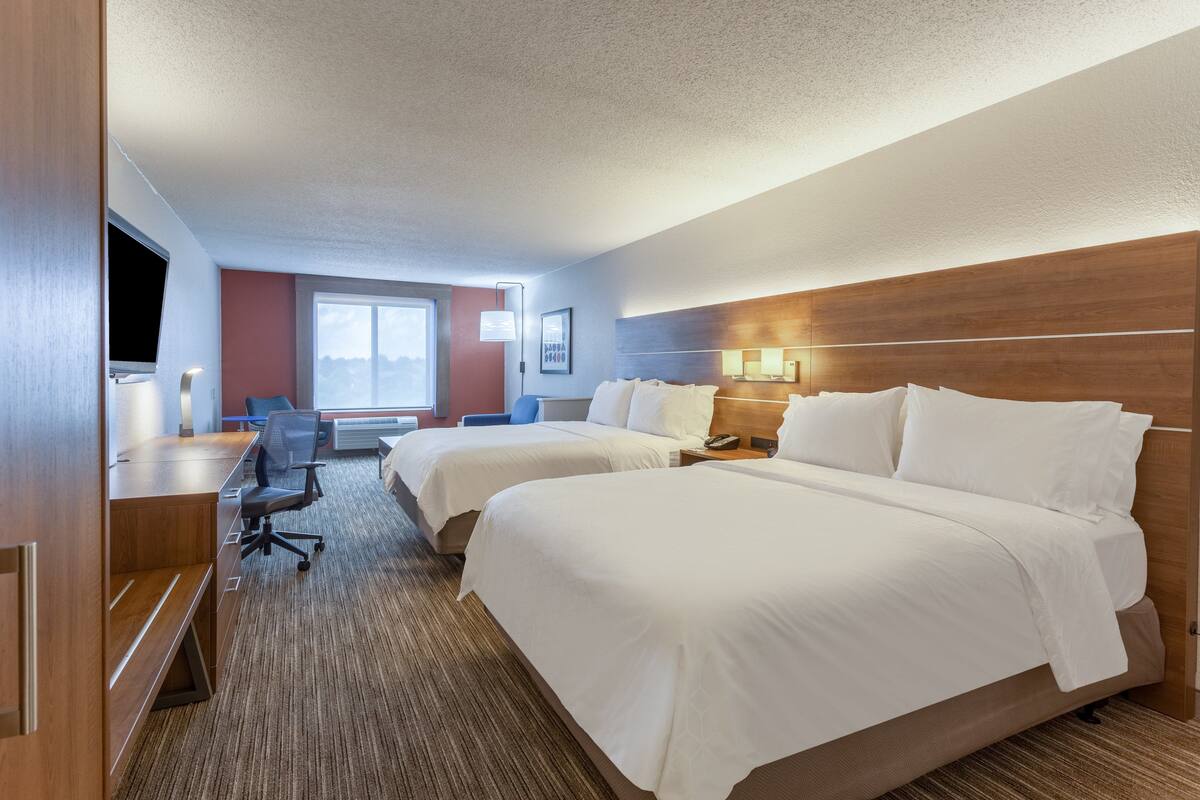 A hotel room with two beds, a desk, a chair, a TV, and a window with a view.