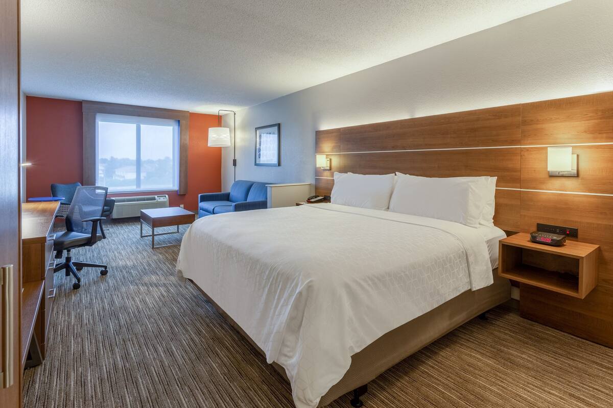 A hotel room with a large bed, a desk, a chair, and a small table.
