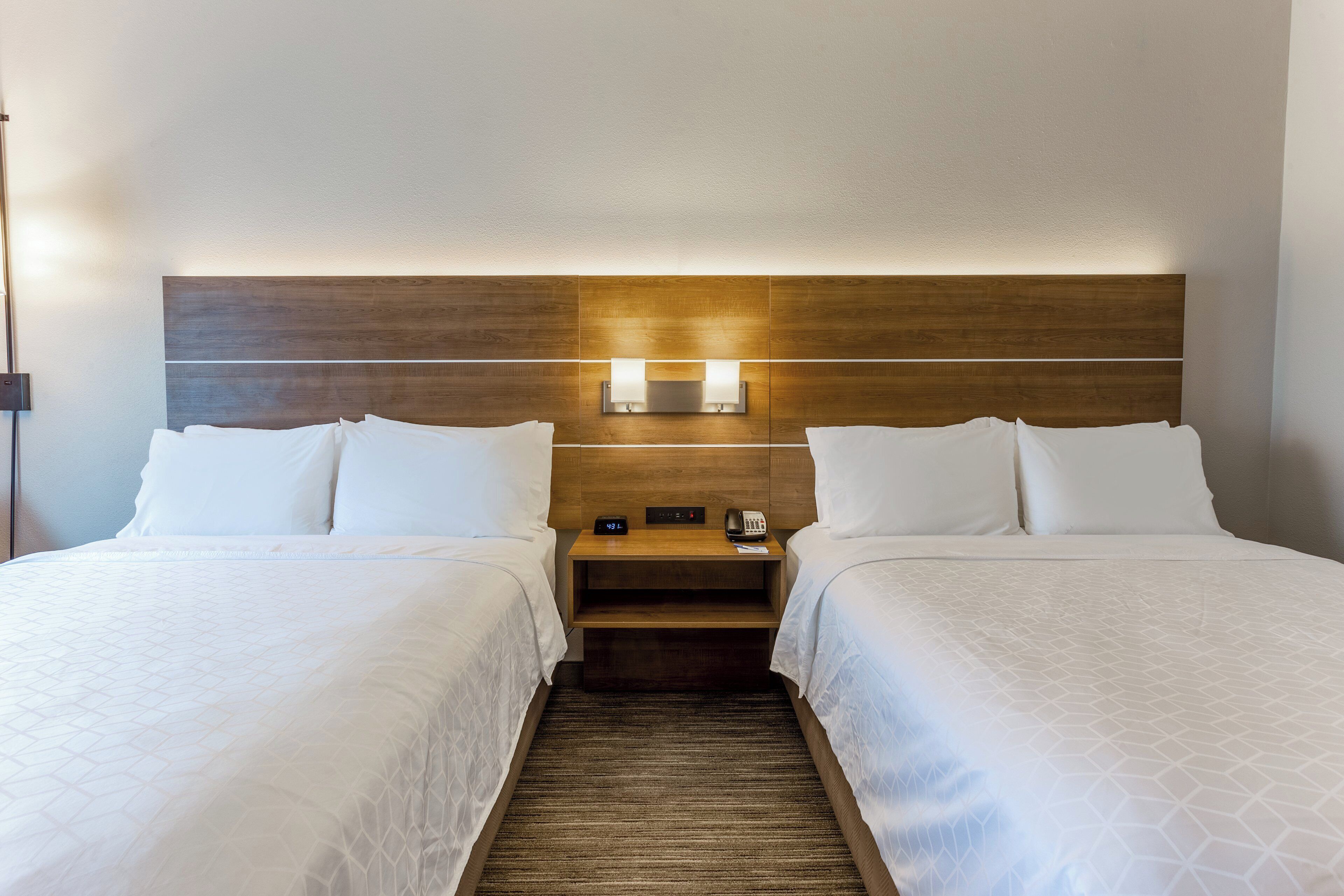 A hotel room with two beds, a wooden headboard, bedside lamps, and a nightstand with a phone.