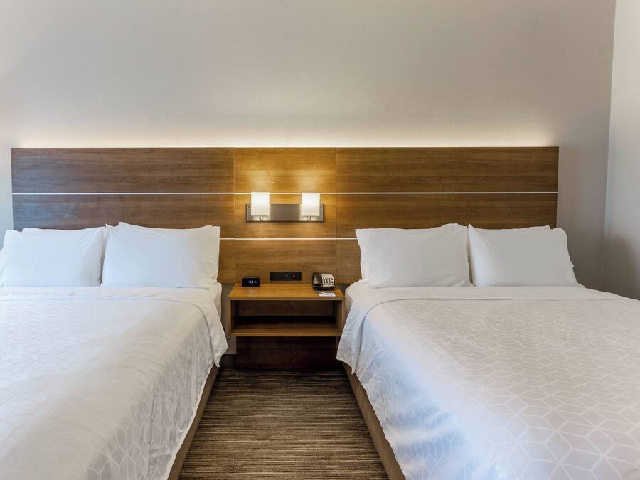 A hotel room with two beds, a wooden headboard, bedside lamps, and a nightstand with a phone.