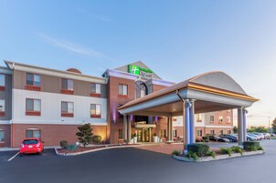 Un hotel Holiday Inn Express & Suites con entrada cubierta, varios espacios de estacionamiento y un automóvil rojo estacionado frente.